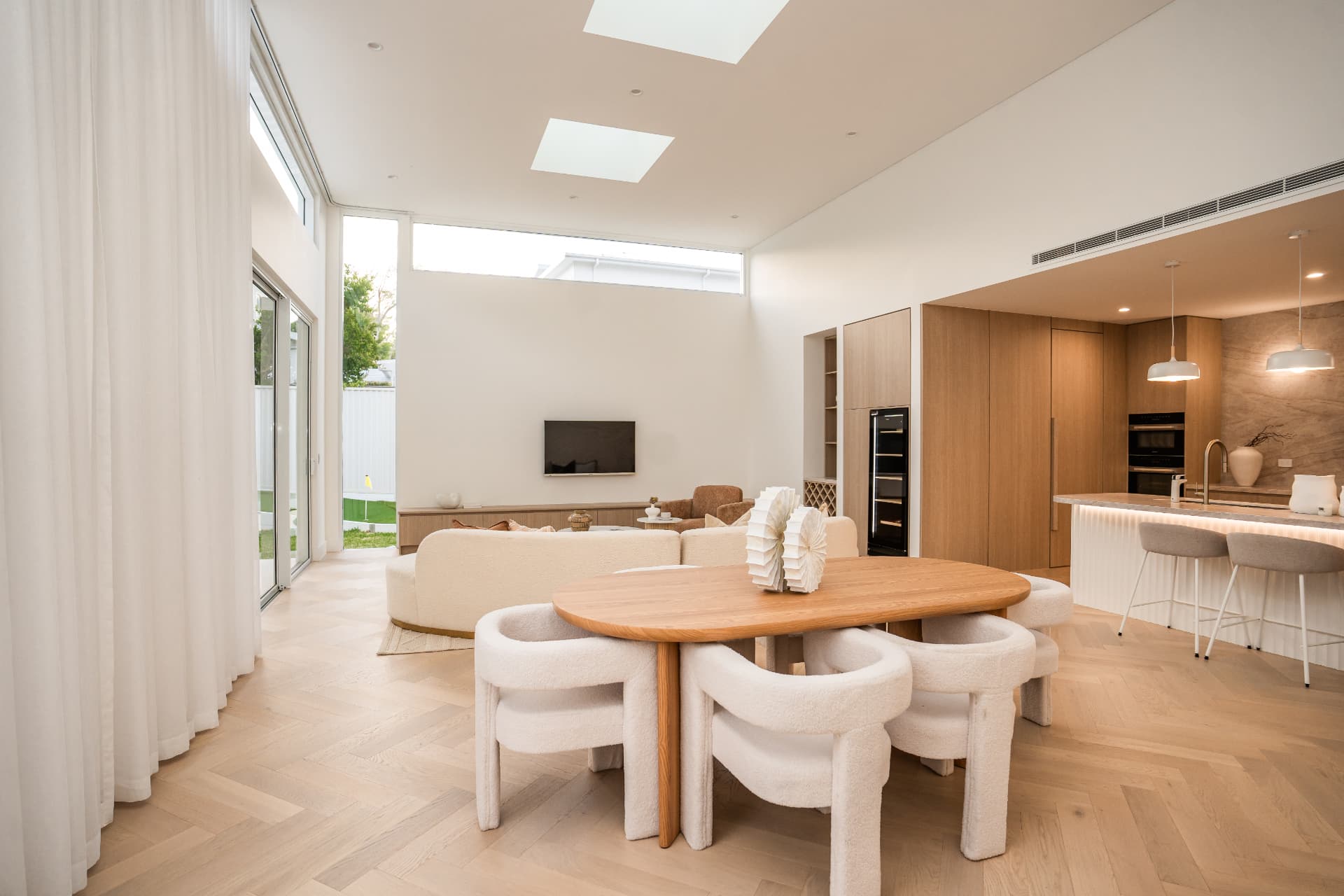 Dining and living space with skylights, oak table, herringbone floors and the kitchen beyond