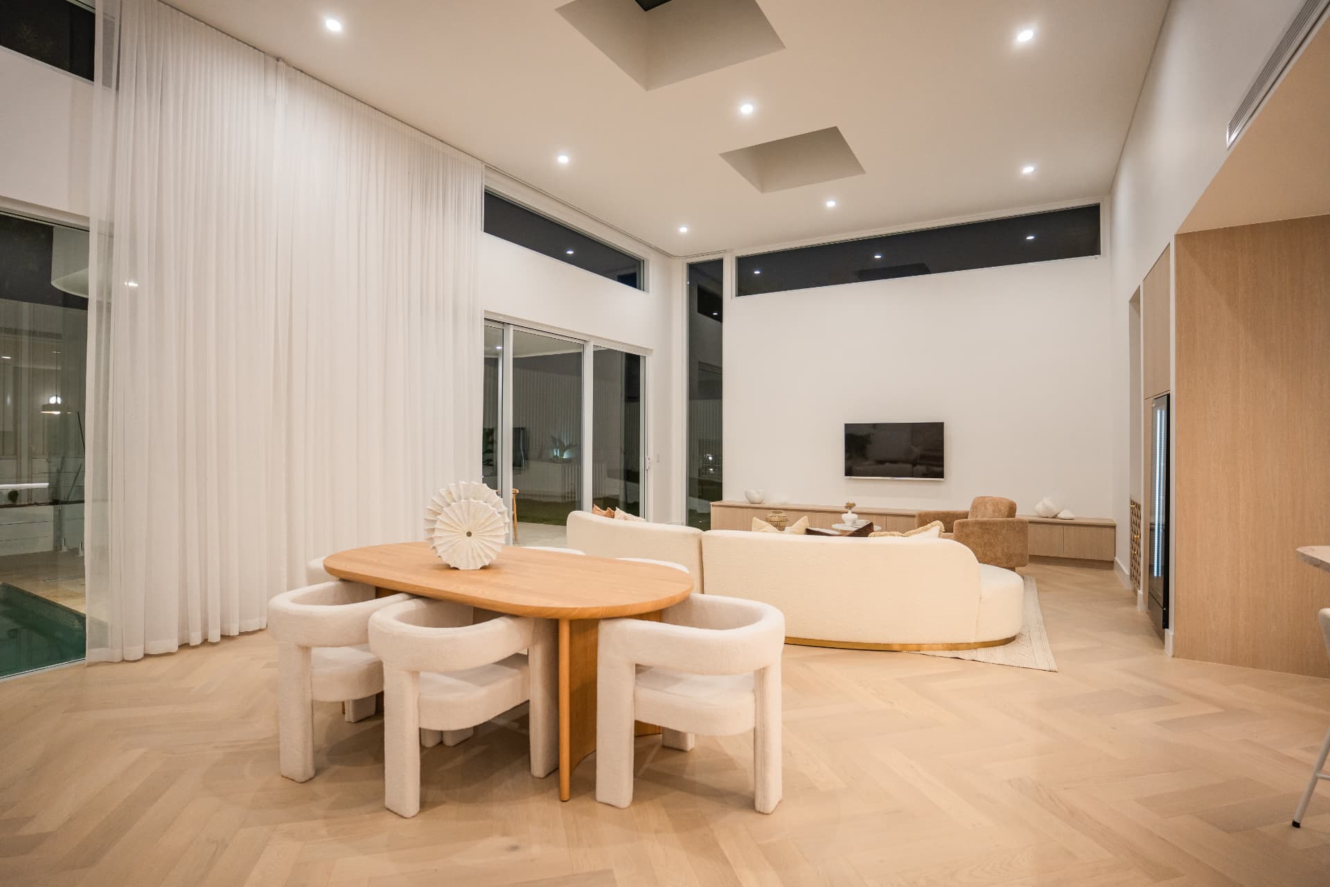 Double-height dining and living area at night with oak table, boucle chairs, curved sofa and herringbone floors