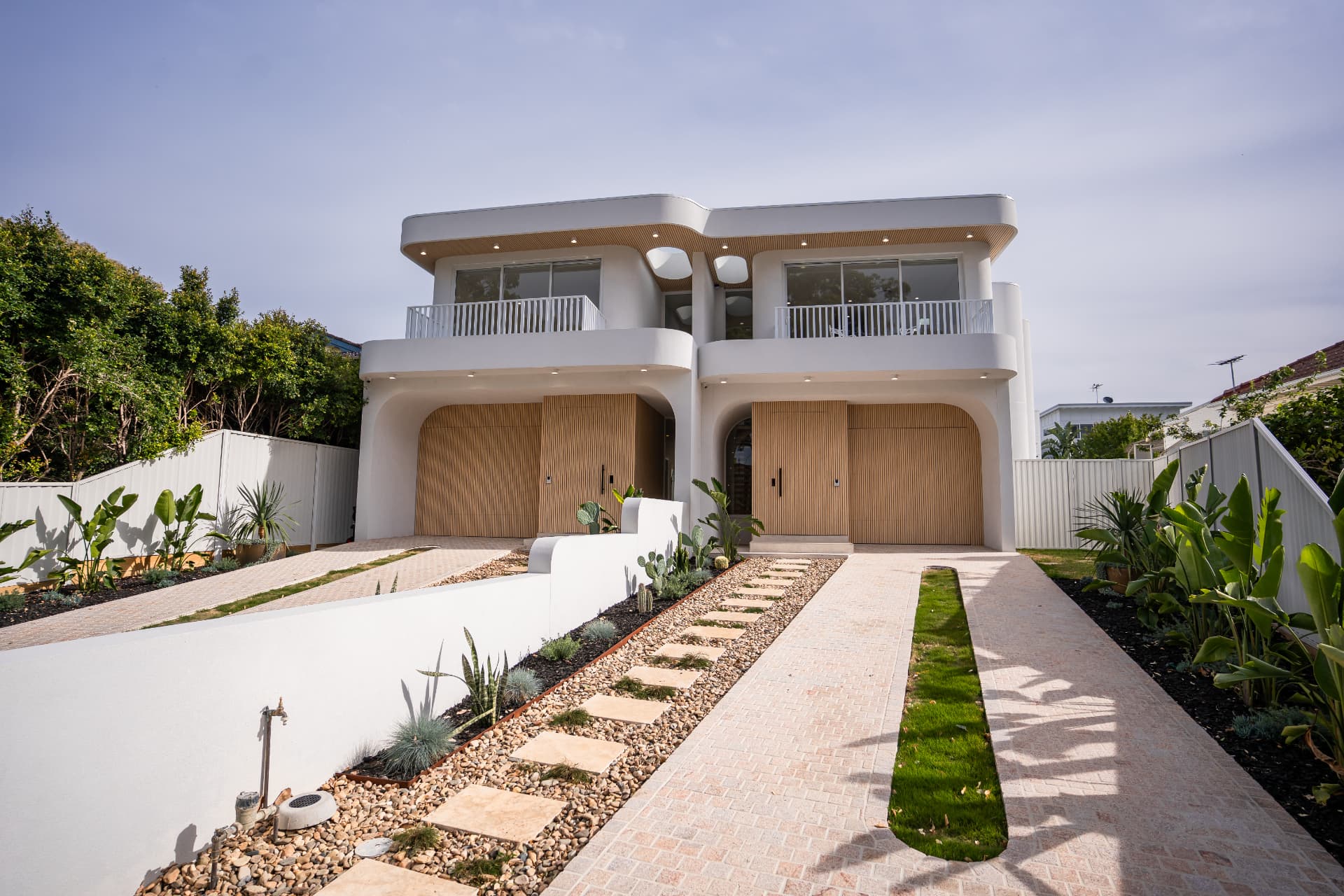 Completed Cronulla duplex with curved white rendered facade, battened timber garage doors and landscaped driveway