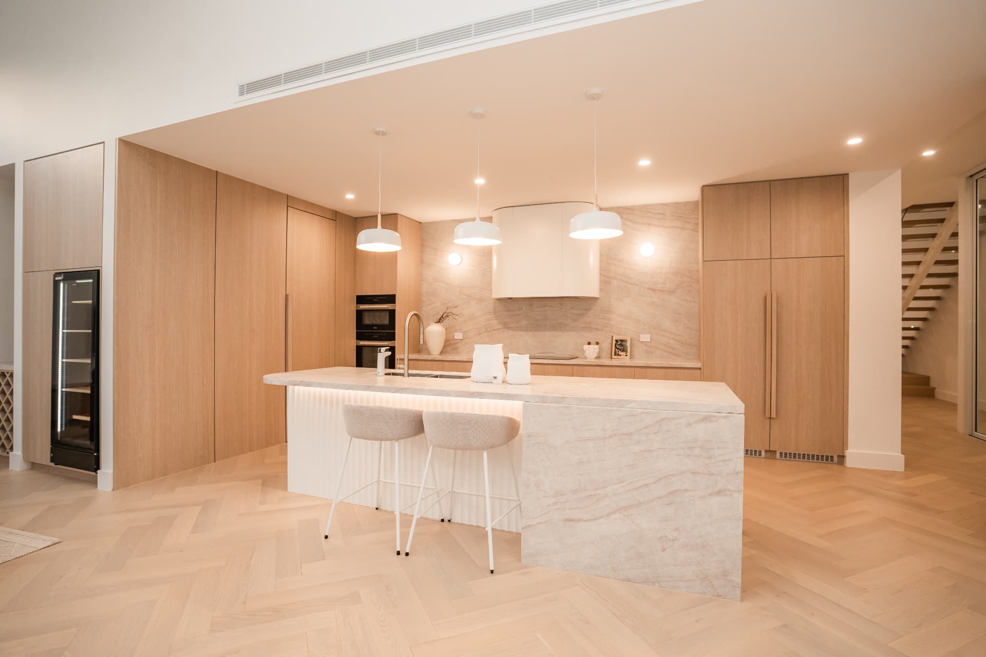 Kitchen with oak joinery, stone island bench, integrated appliances and herringbone oak flooring