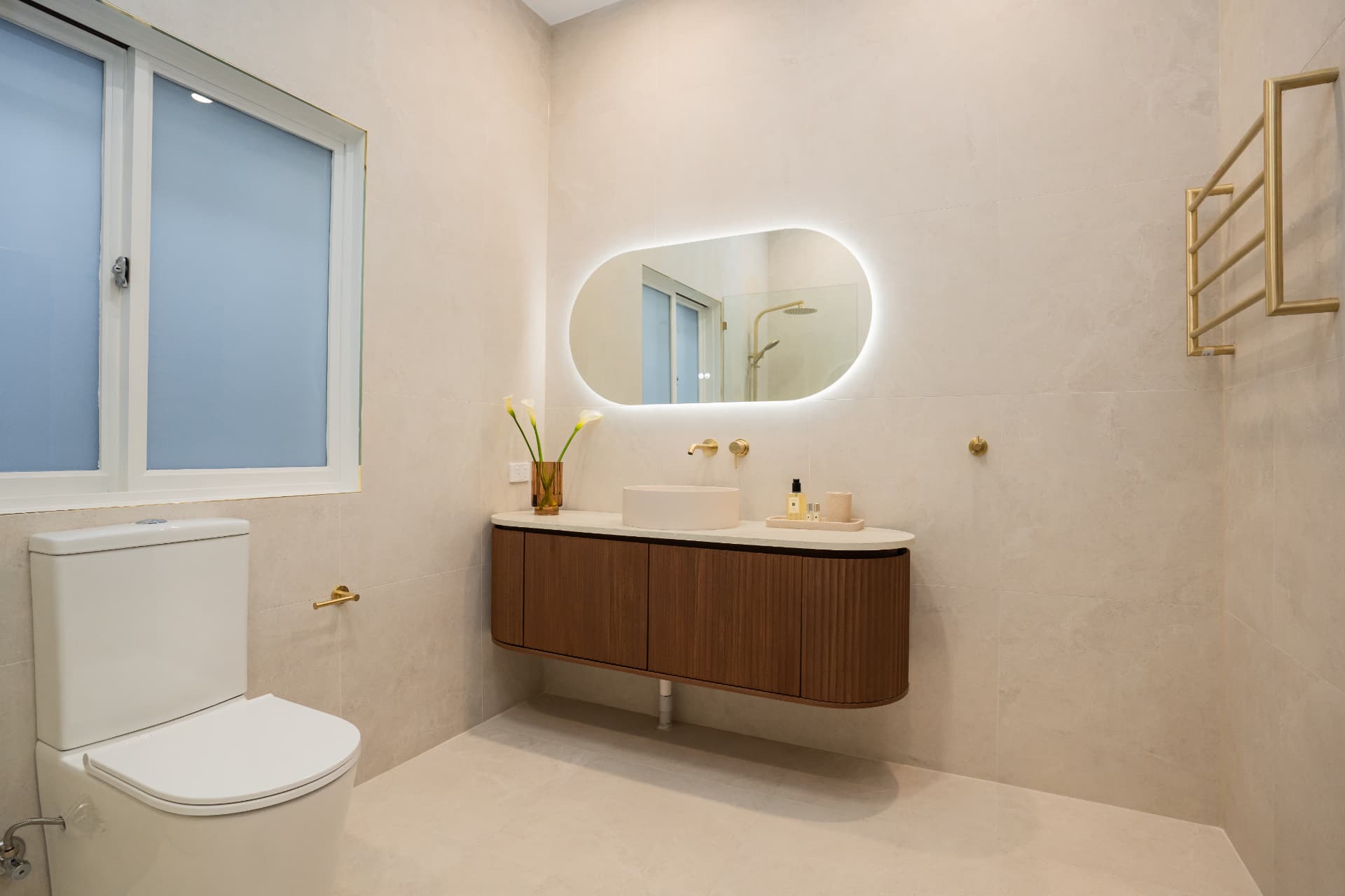 Wide view of the tiled bathroom showing vanity, toilet and heated towel rail