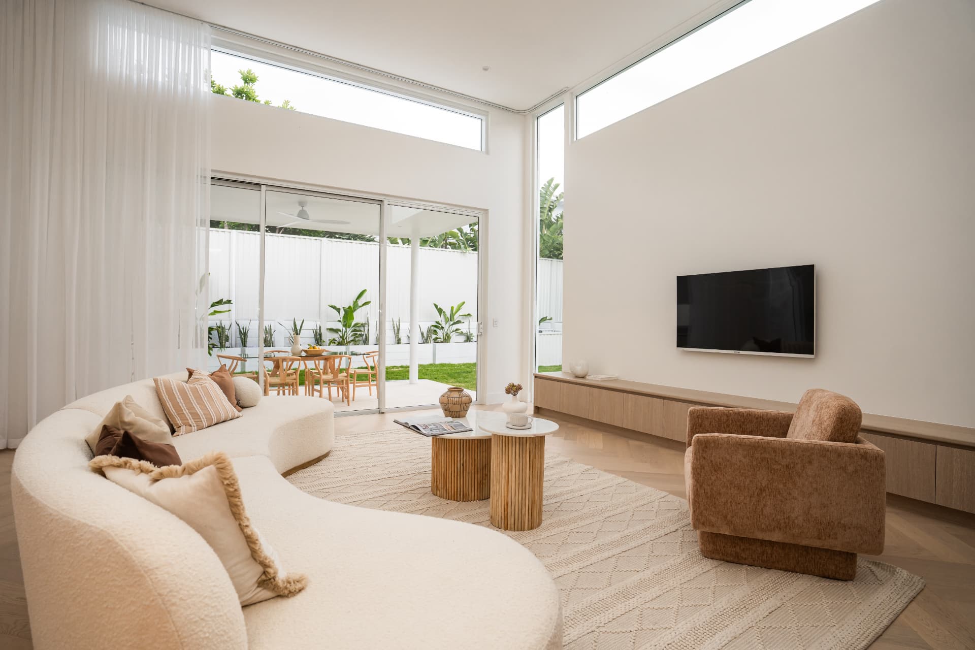 Double-height living room with clerestory glazing, curved sofa and sliding doors to the courtyard
