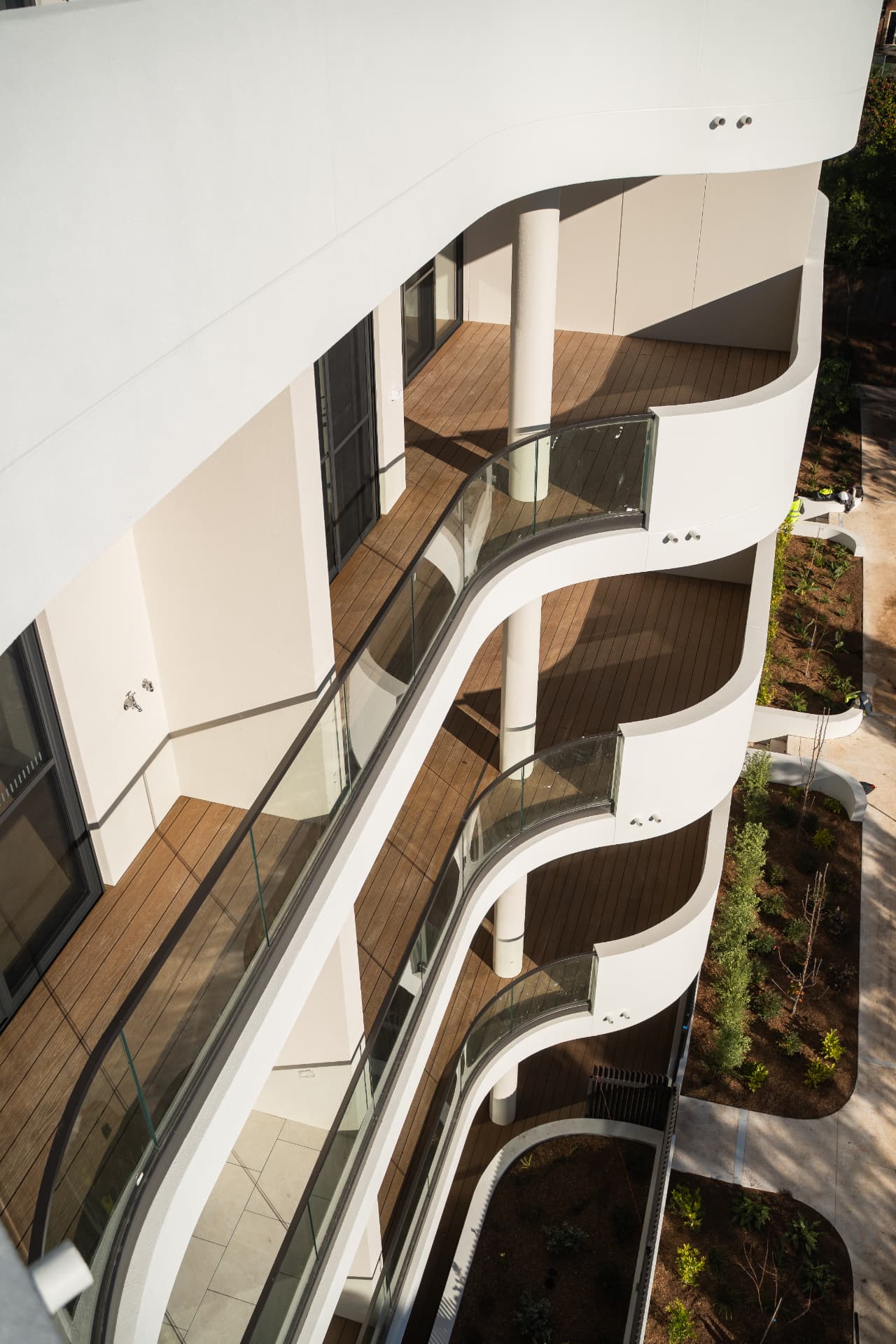 Stacked curved balconies with composite decking and glass balustrades seen from above