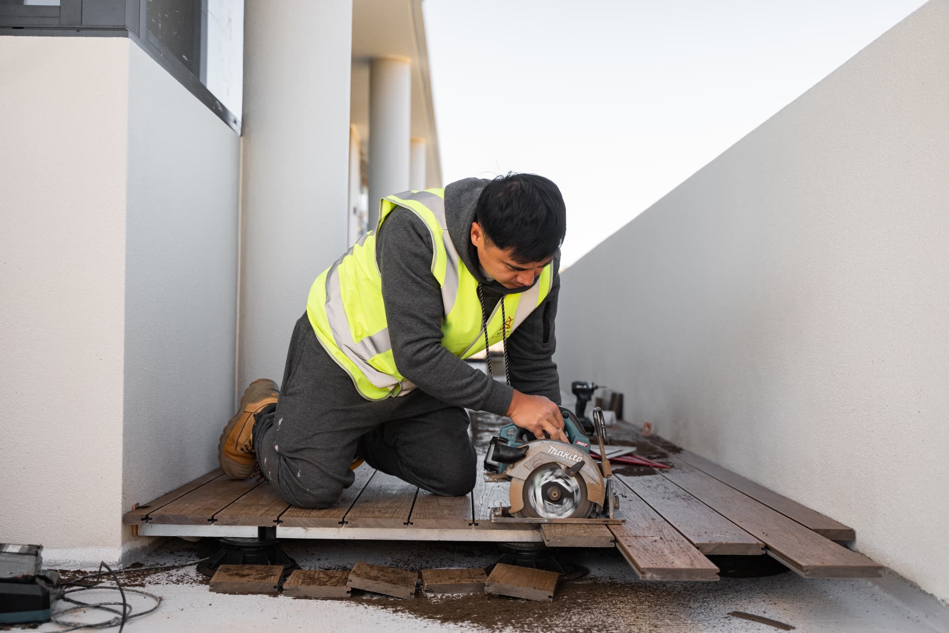 Tradesman in a hi-vis vest cutting composite decking boards with a circular saw on site